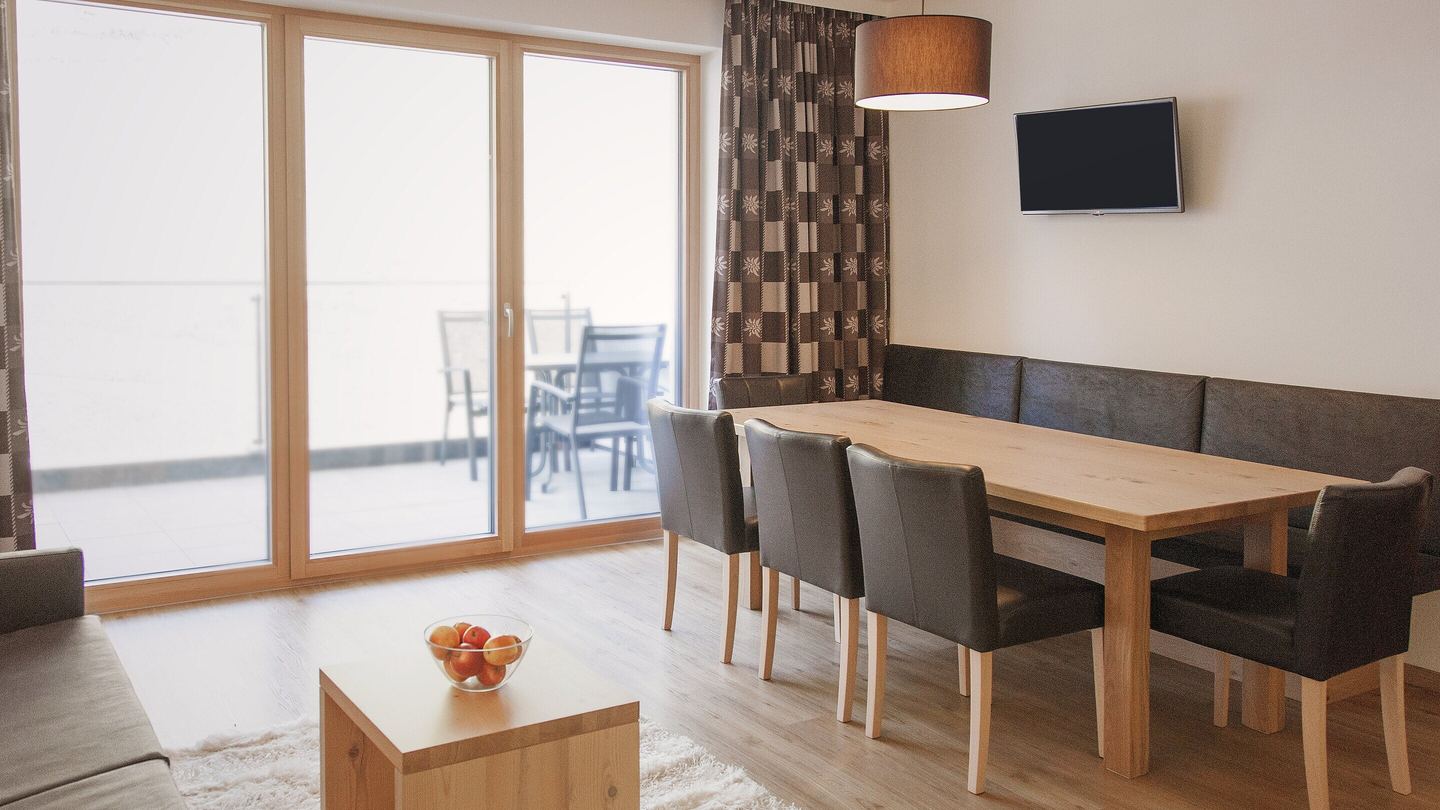 Wohnraum Trisanna bei Tag: große Fensterfront zur Terrasse, langer Esstisch mit Eckbank